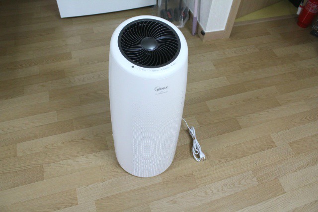 바닥에 놓인 흰색 원기둥 형태의 위닉스 공기청정기 본체 전면 모습