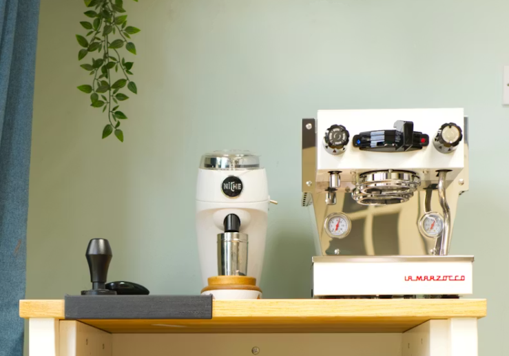 가정용 커피머신과 전동 그라인더가 나무 선반 위에 정갈하게 놓여 있는 홈카페 공간