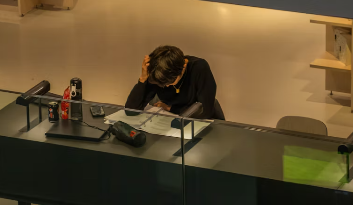 지친 표정으로 책상에 앉아 머리를 감싸고 있는 사람, 피로와 스트레스를 나타내는 장면