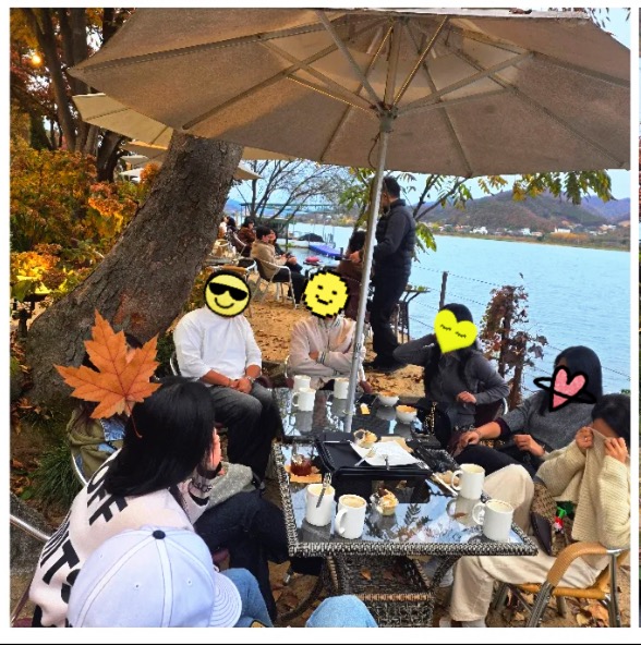포천 데너리스 강 앞 야외석에서 가을 풍경을 보며 모여 앉아 있는 일행의 모습. 뒤로 북한강과 산이 펼쳐진 장면