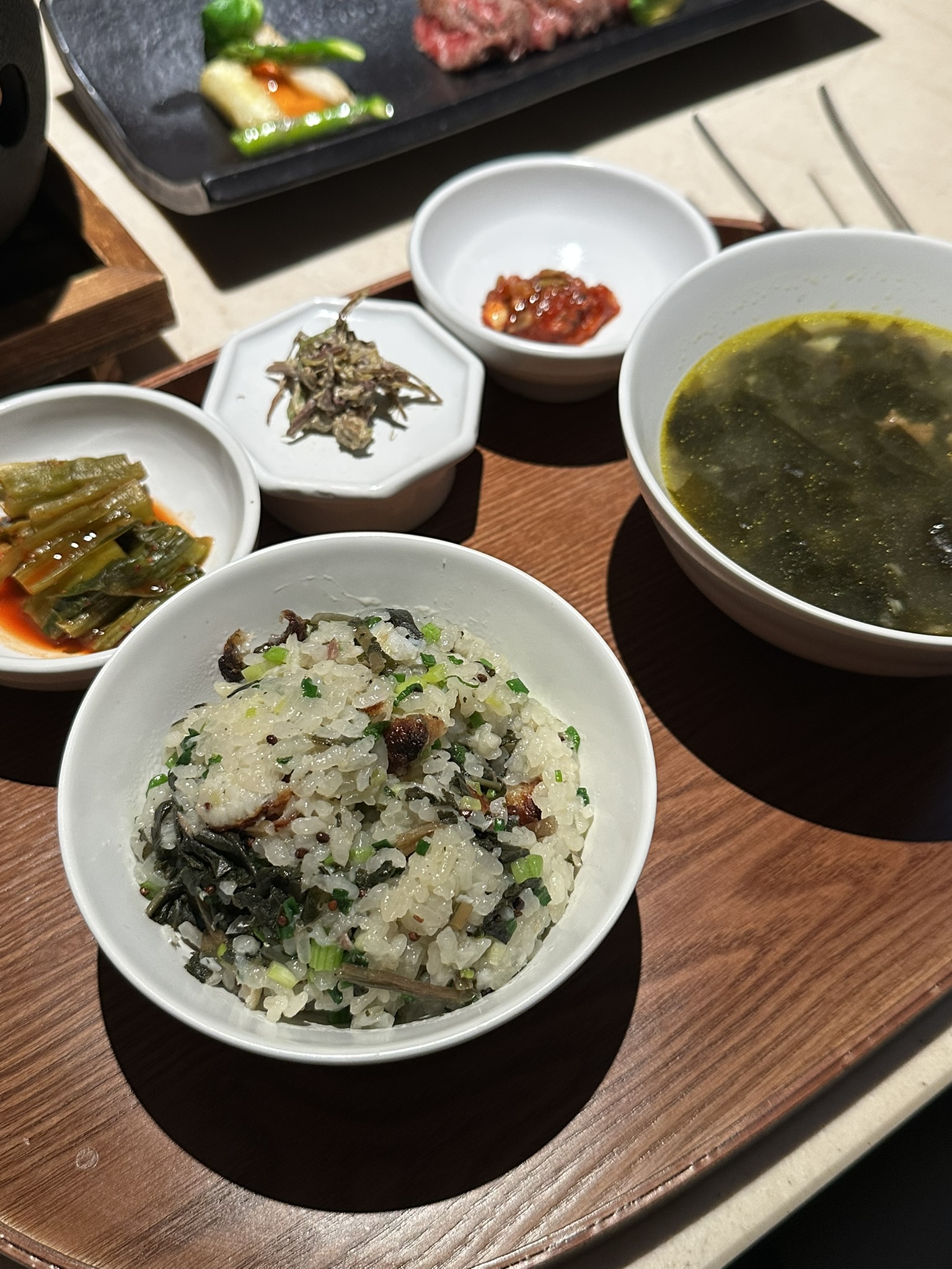 밑반찬인 갓김치, 고사리, 씨앗젓갈과 한우 미역국, 농어 솥밥이 차려진 반상 사진