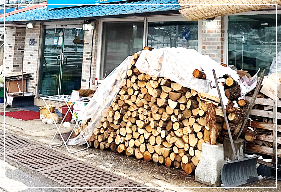 매장 입구에 참나무 장작들이 수북하게 쌓여 있는 고창 장작 난로 삼겹살 맛집 외관