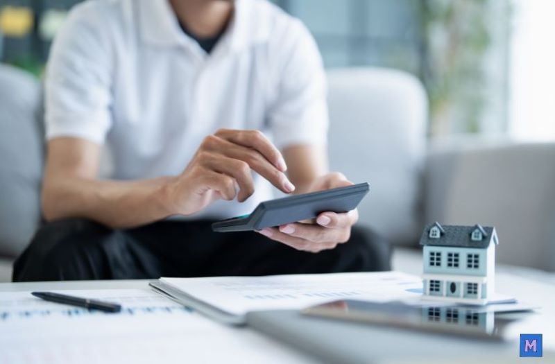 근로장려금 신청을 위해 홈택스 모바일 앱으로 계산하는 사람의 손과 집 모형이 있는 책상 canva