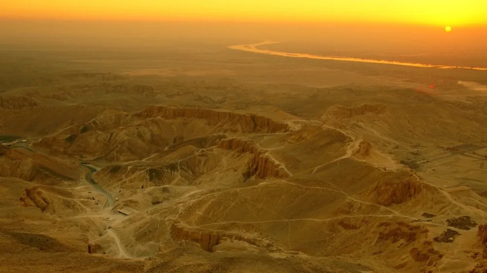 이집트 룩소르 서쪽의 밸리 오브 더 킹즈를 석양이 비추는 장면, 굽이치는 산과 협곡 사이로 무덤 진입로가 보인다.