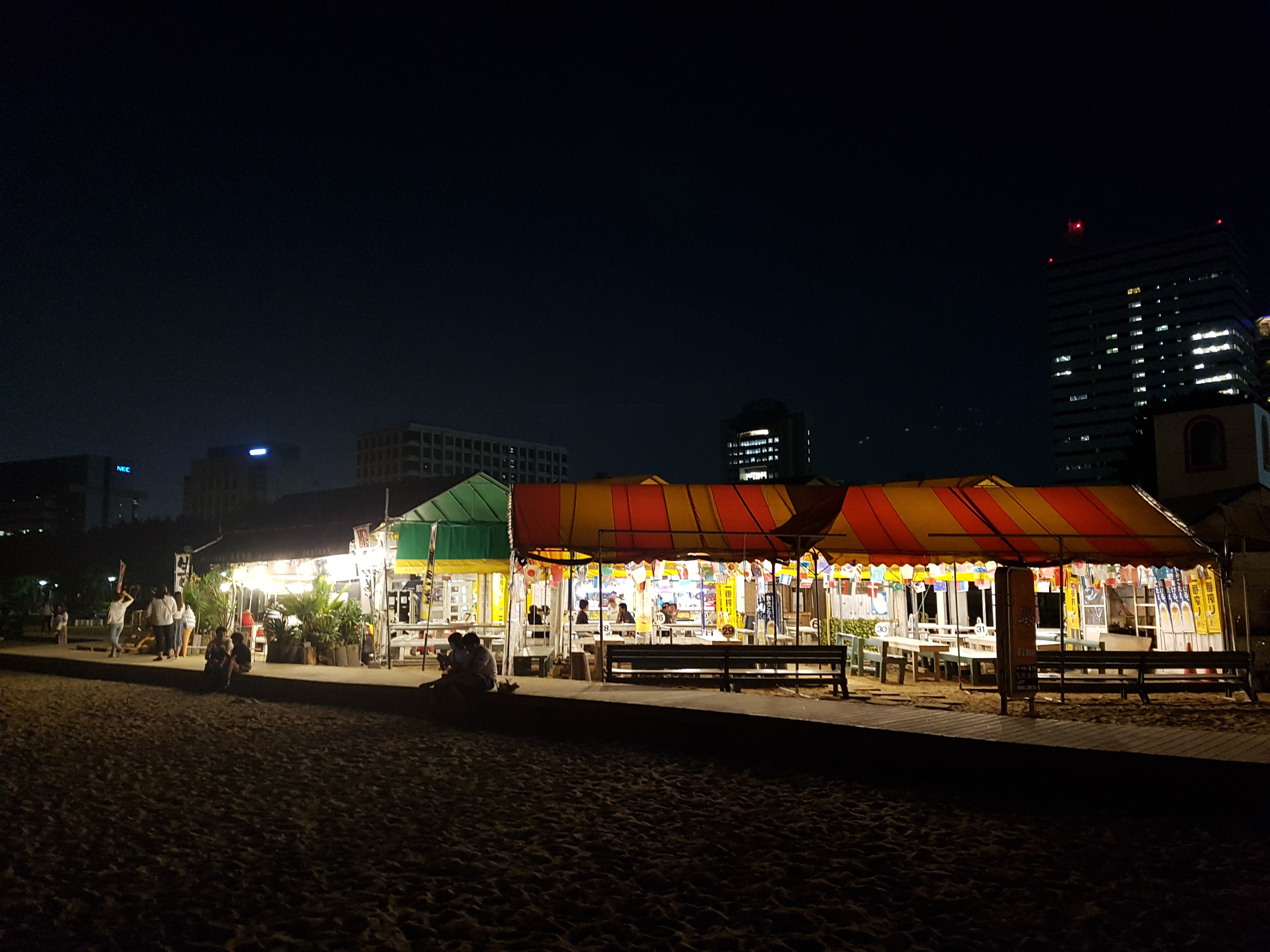 밤이 되어 조명이 환하게 밝혀진 모모치 해변의 노천 식당과 포장마차 거리 풍경.