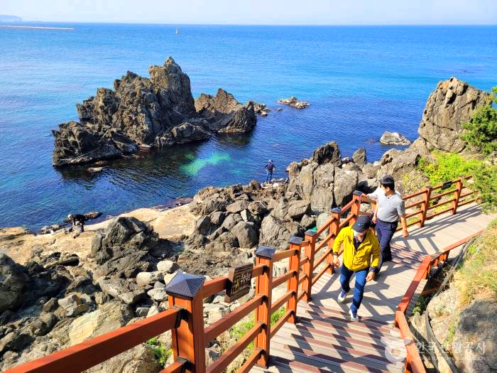 바다옆 산 정상으로 오르는 계단 길에 두 남자가 걸어가고 있다.