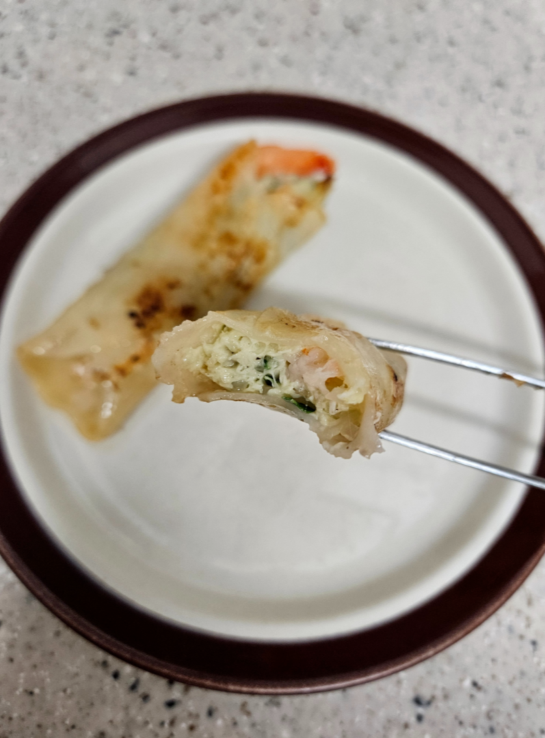 프라이팬에 조리한 비비고 통새우만두를 접시에 담아 반으로 자른 단면에서 속재료와 새우가 보임