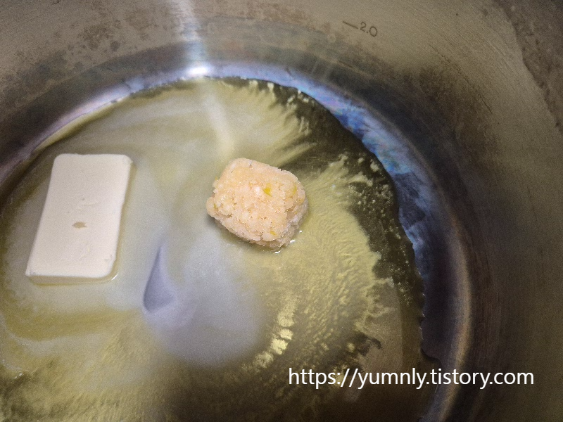 Minced garlic being added to a mixture of melted butter and olive oil in a large pot