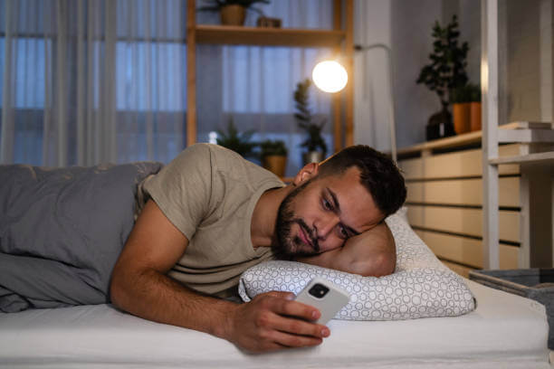 불면증을 유발하는 스마트폰 사용 습관으로 침대에 누워서 화면을 보는 남자의 모습