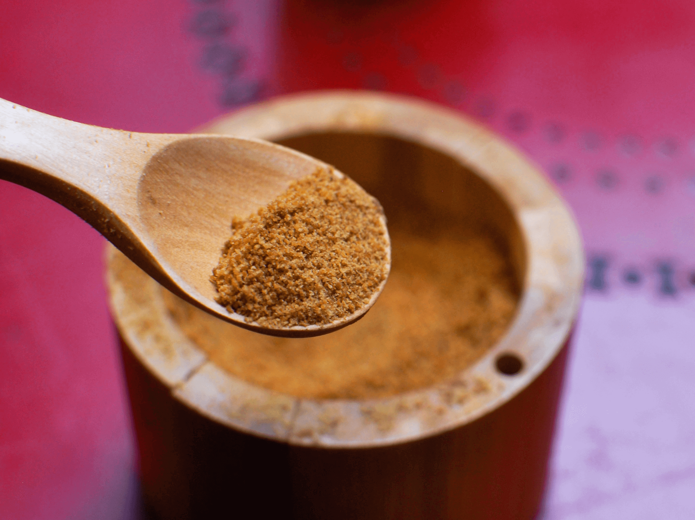 코코넛 규가가 나무 그릇에 담겨졌다. 나무 숟가락으로 갈색의 설탕을 약간 뜬 모습이다.