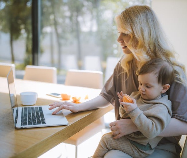 아이를 안고 노트북으로 일을하고 있는 여성의 사진