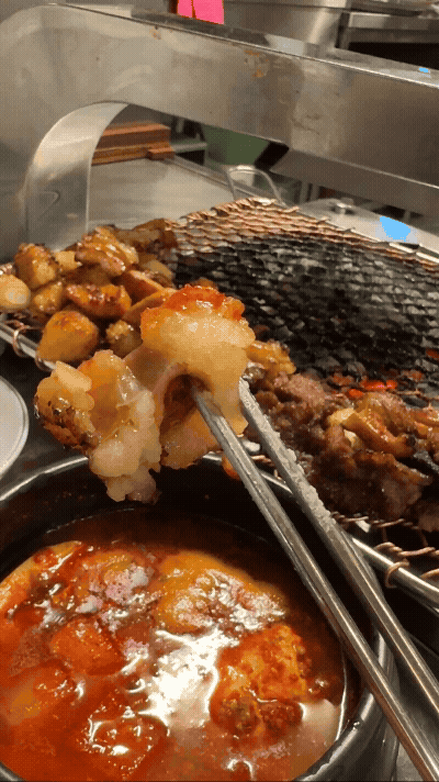 세광양대창 정자점에서 젓가락으로 대창을 집어 매콤한 양념장에 찍는 장면&amp;#44; 윤기와 불향이 어우러진 고소한 대창 클로즈업