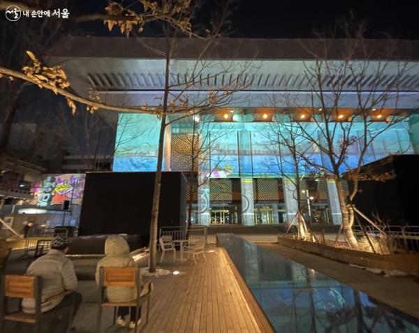 야외 테이블에 자리를 잡고 앉아 화려하고 아름다운 미디어아트를 감상하는 시민들