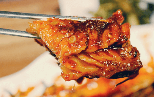 쇠 젓가락으로 코다리조림 한 조각을 들고 있다. 생선살이 가득하고 간장에 잘 조려져 있다.