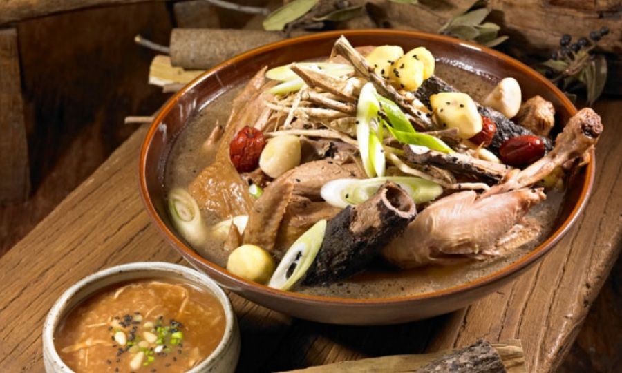 야생에서 체취를 한 닭을 옻나무와 함께 넣어 끓인 옻닭을 나무 테이블 위의 고동색의 동그란 그릇에 가득 담아두고 찍은 사진