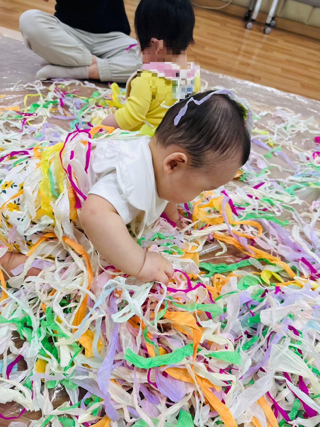 색색의 종이 속에서 엎드린 자세로 습자지를 탐색하며 기어가는 9개월 아기