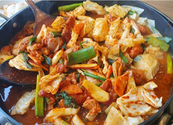 '개수리막국수'의 산골닭갈비 메뉴 사진입니다. 철판위에 닭갈비, 파, 당근, 양배추, 닭갈비를 익히고 있는 사진입니다.