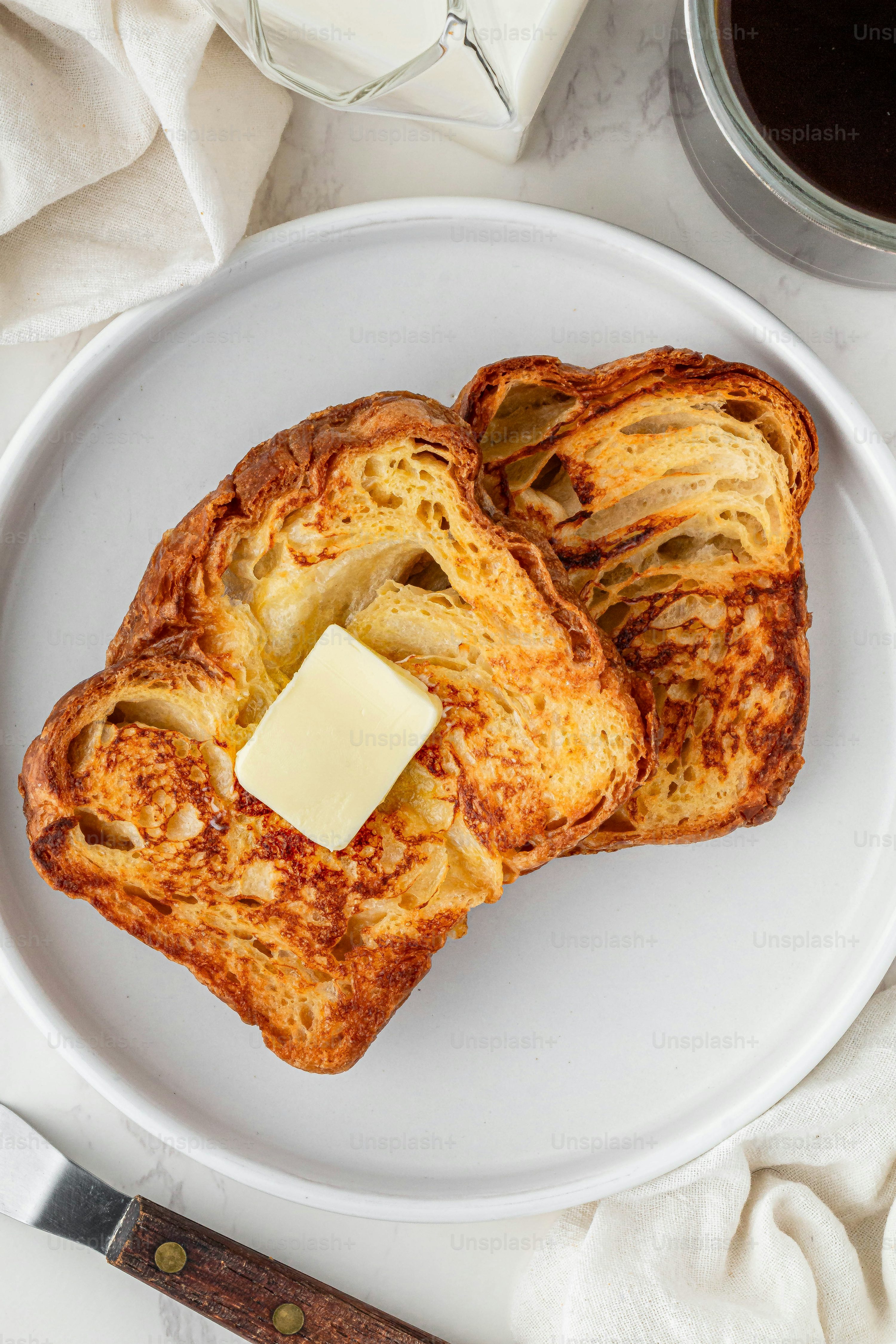 노릇하게 구운 프렌치 토스트 위에 버터 한 조각이 올려진 아침 식사