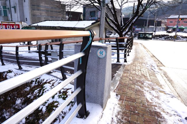 다리 난간 기둥에 붙은 스티커 화살표, 우측 도로에 하얗게 쌓인 눈, 가운데 인도에는 반쯤 녹은 길,