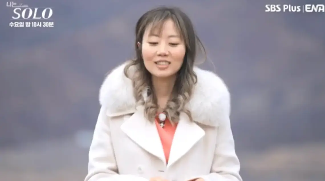 야산배경 흰 털이달린 코트를 입고 웃으며 말하는 옥순