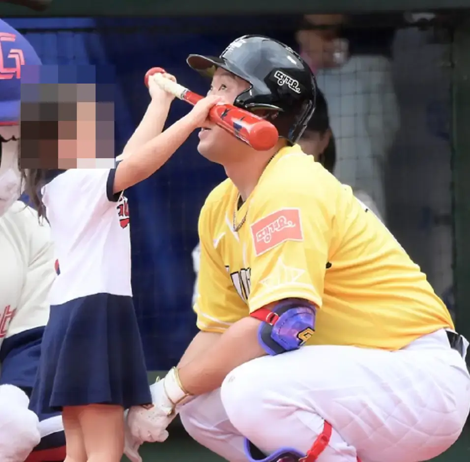 노란옷을 입은 선수를 어린아이가 붉은 방망이로 장난하는 이미지