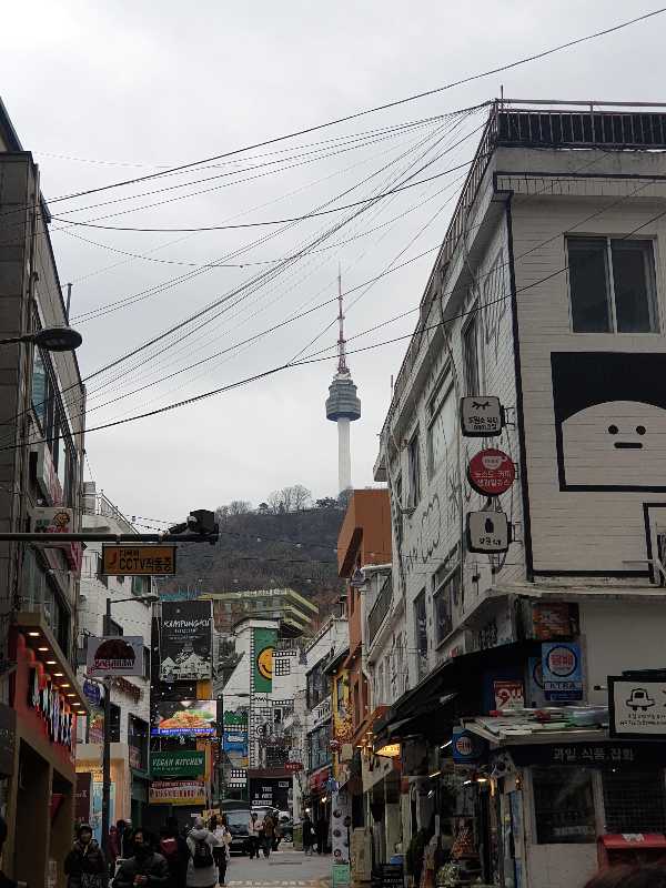 명동 골목 여러 매장들이 이어져있다. 멀리 남산타워가 보인다.