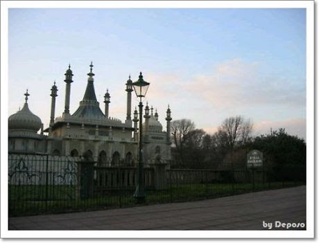 영국 브라이턴의 로열 파빌리온 외관. 인도-이슬람풍의 돔과 첨탑이 돋보이며, 고풍스러운 가로등과 "Royal Pavilion Gardens" 표지판이 조화를 이루고 있다. 저녁 하늘 아래, 정원과 건물이 고요하게 어우러져 이국적이고 낭만적인 분위기를 자아낸다.
