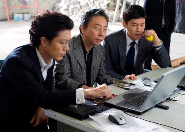 영화 《작전》에서 주식 시장의 흐름을 조작하려는 세 인물이 진지하게 작전을 모의하는 장면. 숫자 뒤에 감춰진 탐욕과 속임수의 세계를 날카롭게 그려낸다.