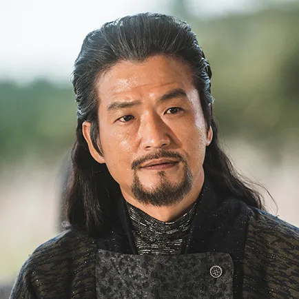 반백의 긴머리를 뒤로 묶은 중년 남자가 짙은 회색 비단옷을 입고 있는 드라마 아라문의 검 아사필 캐릭터