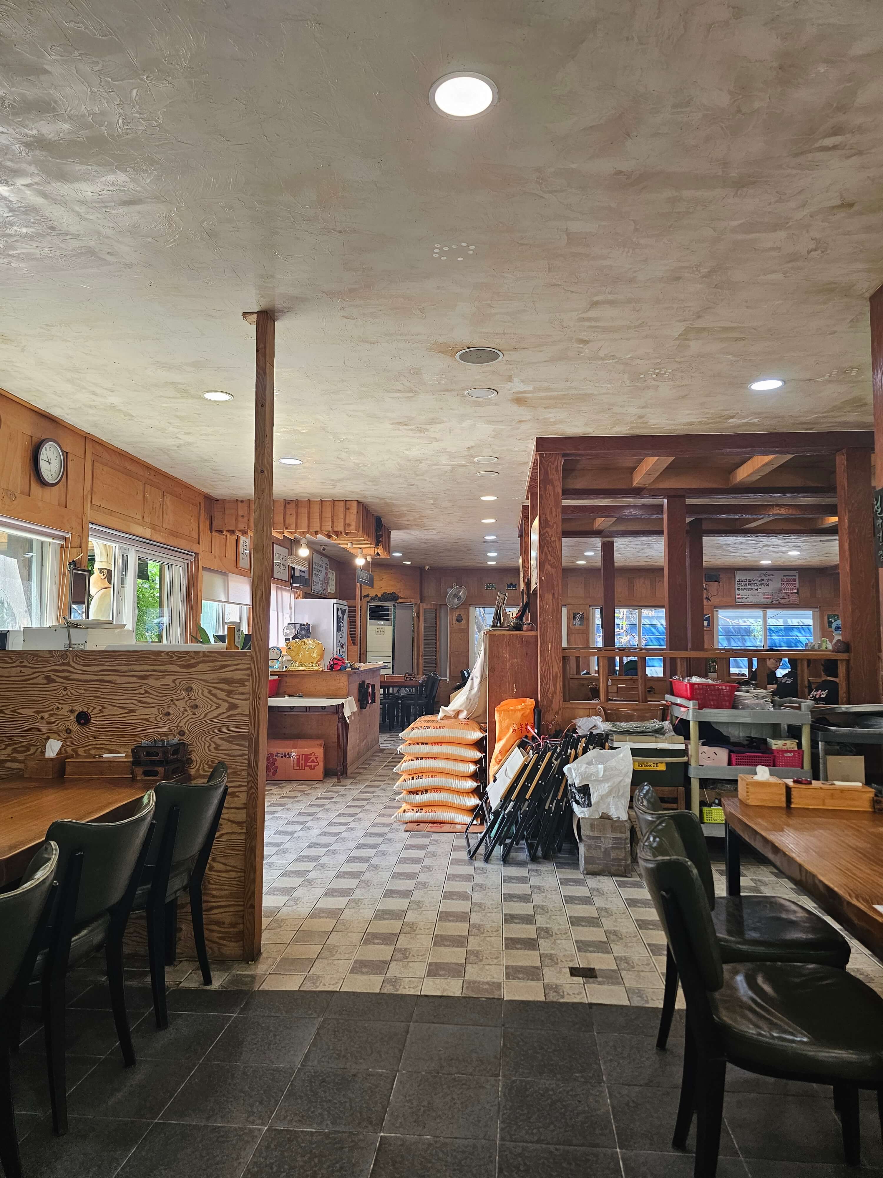 넓은 연입밥 집의 내부 사진이 보입니다 나무로된 기둥이 있고 정괄하게 의자와 쌓아놓은 쌀들이 보입니다.