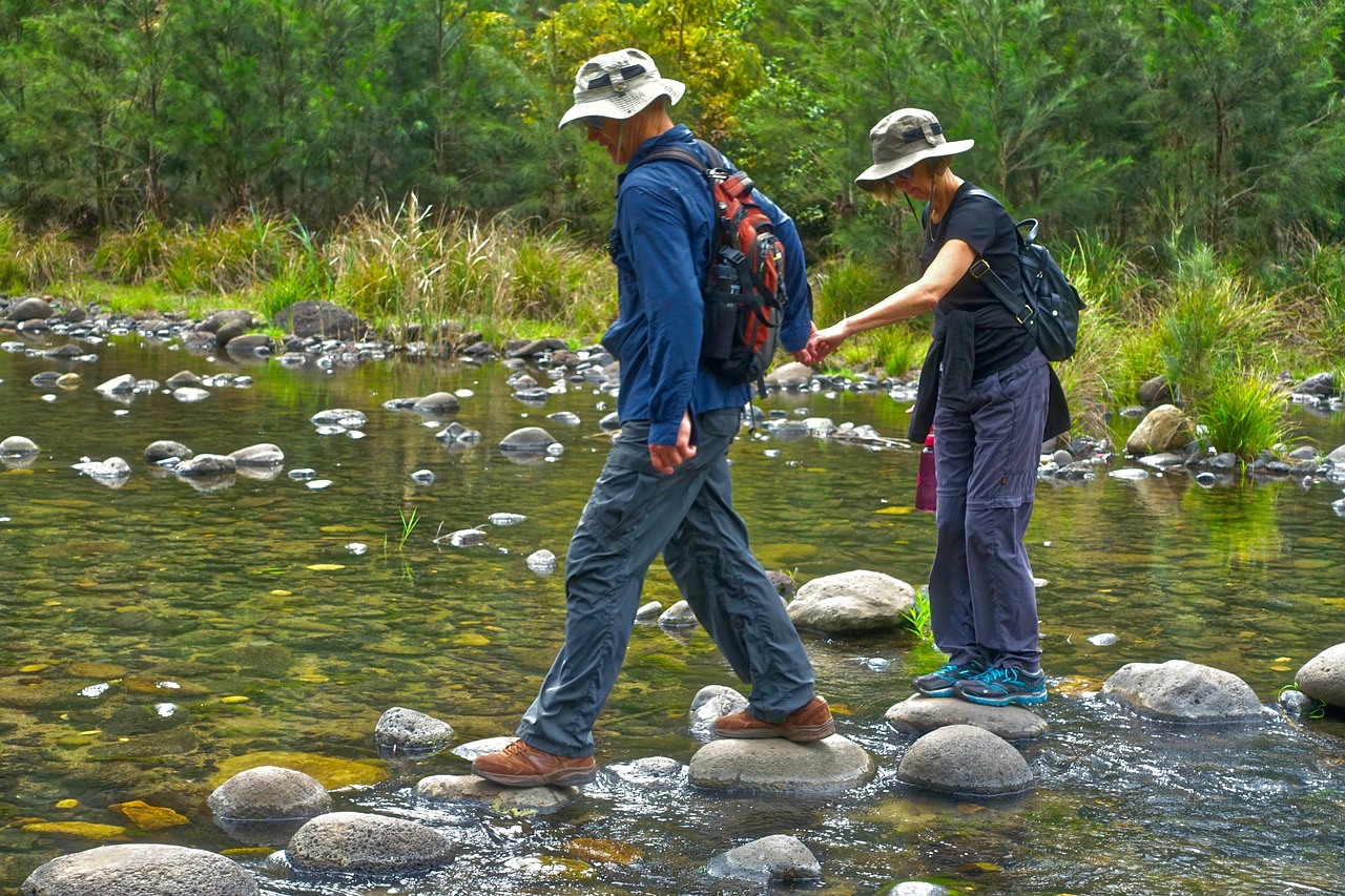 냇물의 바위를 중년부부가 손을 잡고 건너고 있는 사진