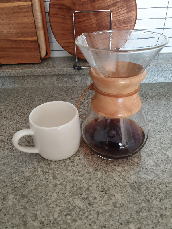 테이블 위에 컵과 추출된 커피가 담긴 케멕스 드리퍼가 놓여 있다.