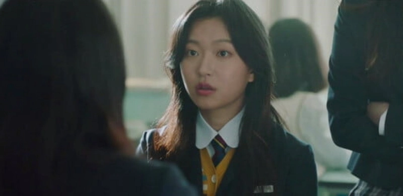 고등학교 교실을 배경으로 교복을 입고 긴머리를 하고 앉아 있는 국민사형투표의 혜미 캐릭터