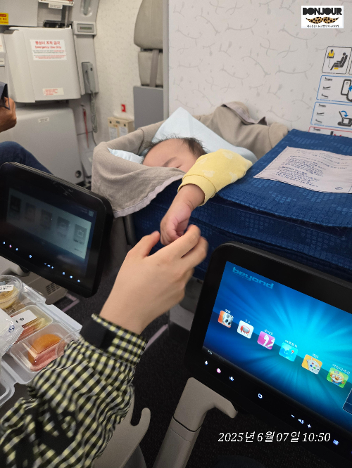 베시넷에 잠들어있는 10개월 아기와 맞은편에서 기내식 식사중인 부모