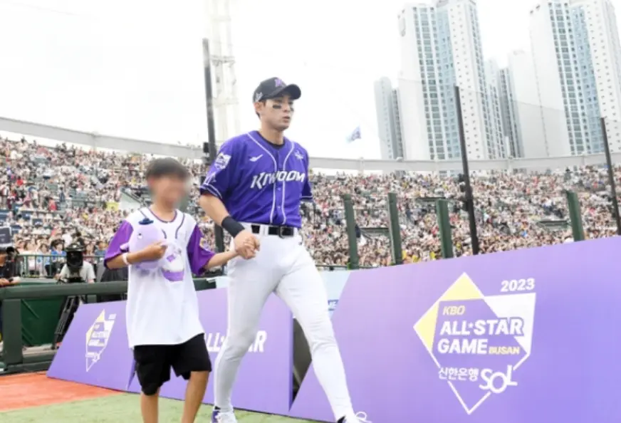 보라색흰바지 유니폼을 입은 선수가 어린이와 손잡고 입장하는 모습