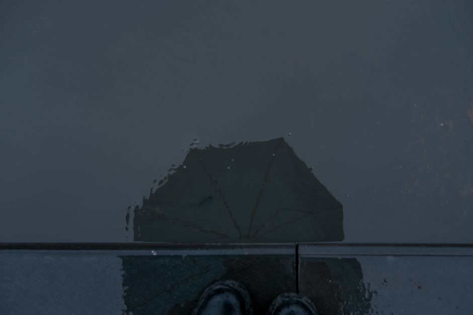 Moody street scene capturing an umbrella's reflection in a puddle.