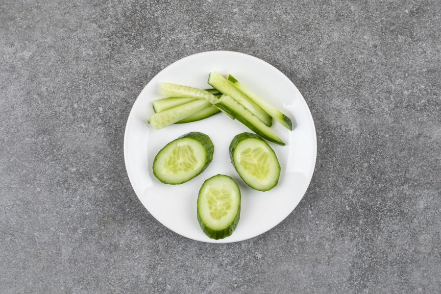 야생에서 채취를 한 오이를 검은 바닥 위에 동그랗고 하얀 접시를 두고 그 위에 썰어 놓은 오이 3개와 오이를 채를 썰어 놓은 것을 두고 위에서 찍은 사진