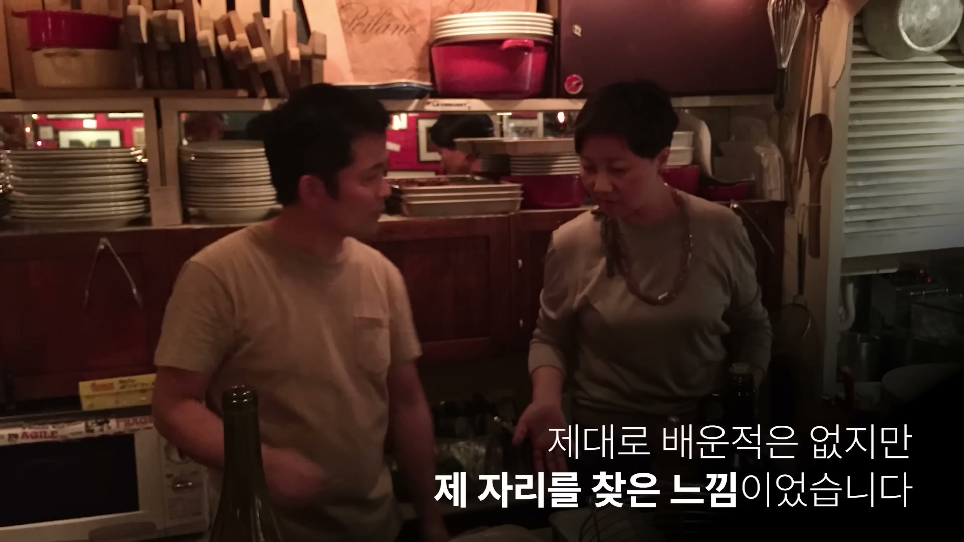 어두운 톤의 식당 부엌에서 셰프 우정욱이 다른 사람과 대화하는 장면.