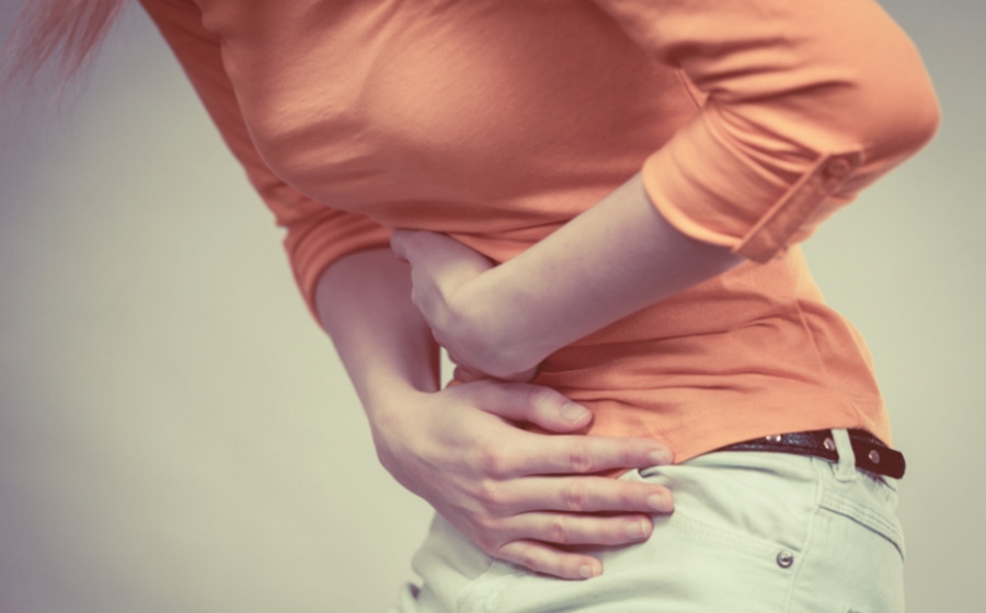 주황색의 윗옷과 흰색의 바지를 입은 여성이 맹장염으로 인한 통증으로 양쪽 손을 복부에 대고 통증을 참고 있는 것을 찍은 사진