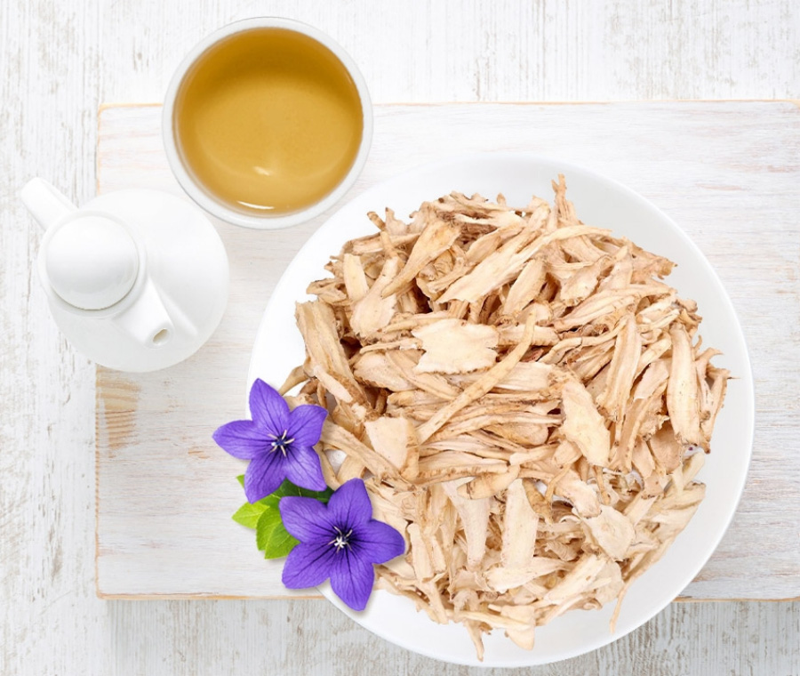 야생에서 채취를 한 도라지 식물의 뿌리인 길경을 깨끗하게 세척을 한 후에 말린 것을 편으로 얇게 썰은 것을 하얀 바닥 위에 도라지차와 주전자, 그리고 동그랗고 하얀 그릇에 가득 담아두고 도라지꽃과 함께 놓아두고 찍은 사진