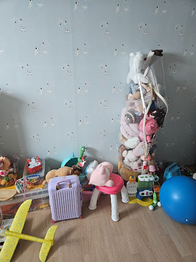 방 한쪽에 정리되지 않은 장난감들이 모여 있는 현실적인 육아 가정의 모습.