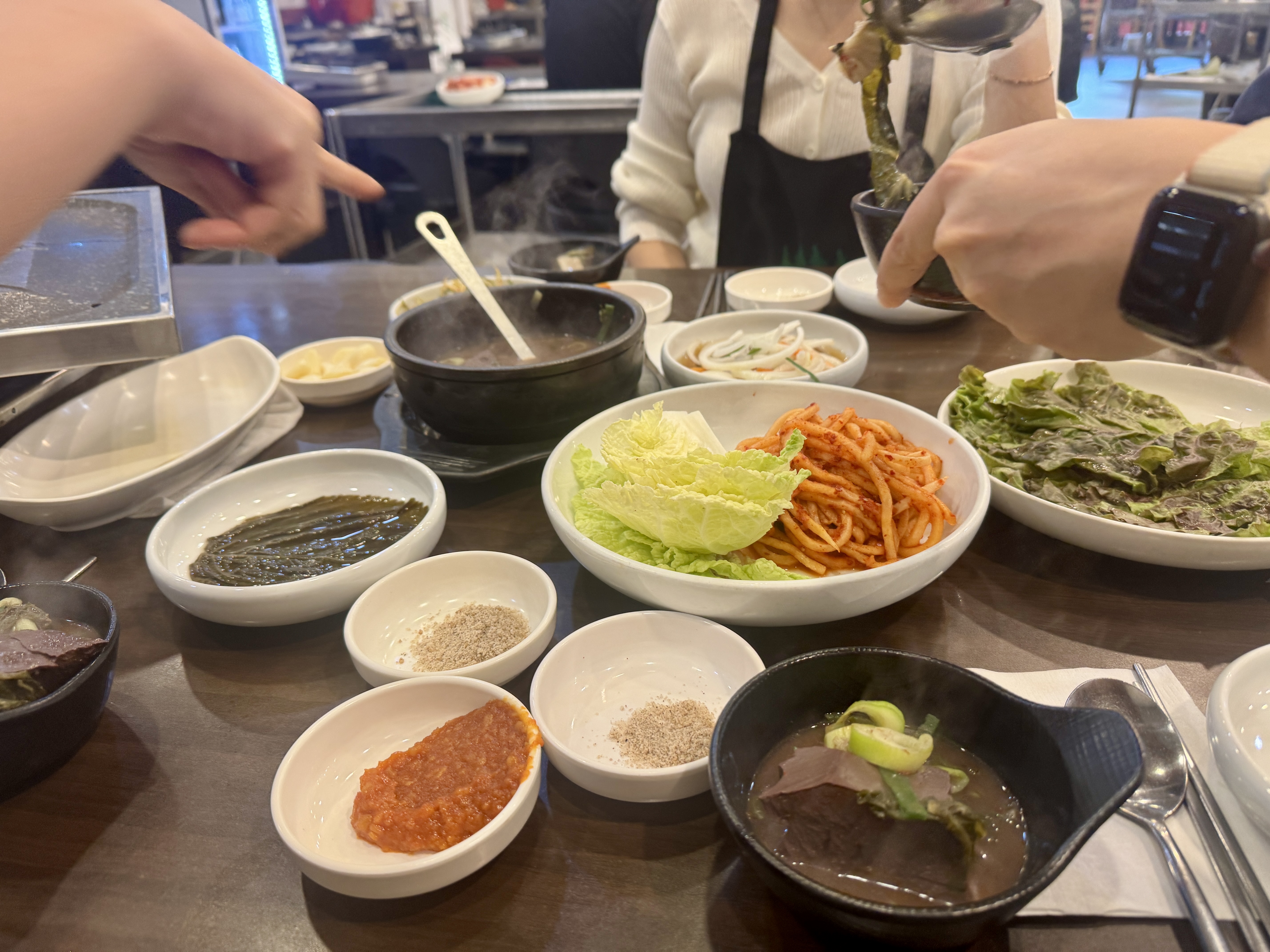 솔밭삼겹살 테이블 전경. 상추&amp;#44; 배추&amp;#44; 무생채&amp;#44; 쌈장 등 밑반찬 구성과 선지해장국이 함께 놓여 있다.