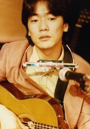 김광석이-목에는-하모니카를-걸고-어깨에-기타를-메고-아련한-눈빛으로-뭔가를-응시하고-있는-사진
