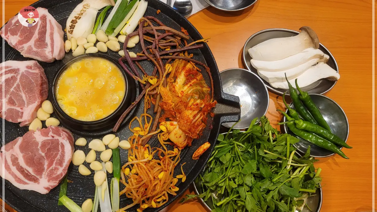 경기-남양주-다산점-효자동솥뚜껑-보리밥집-솥뚜껑-위에 -올려진-생목살과-마늘-김치-등