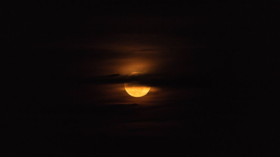 A moody and dramatic shot of the full moon obscured by dark clouds.
