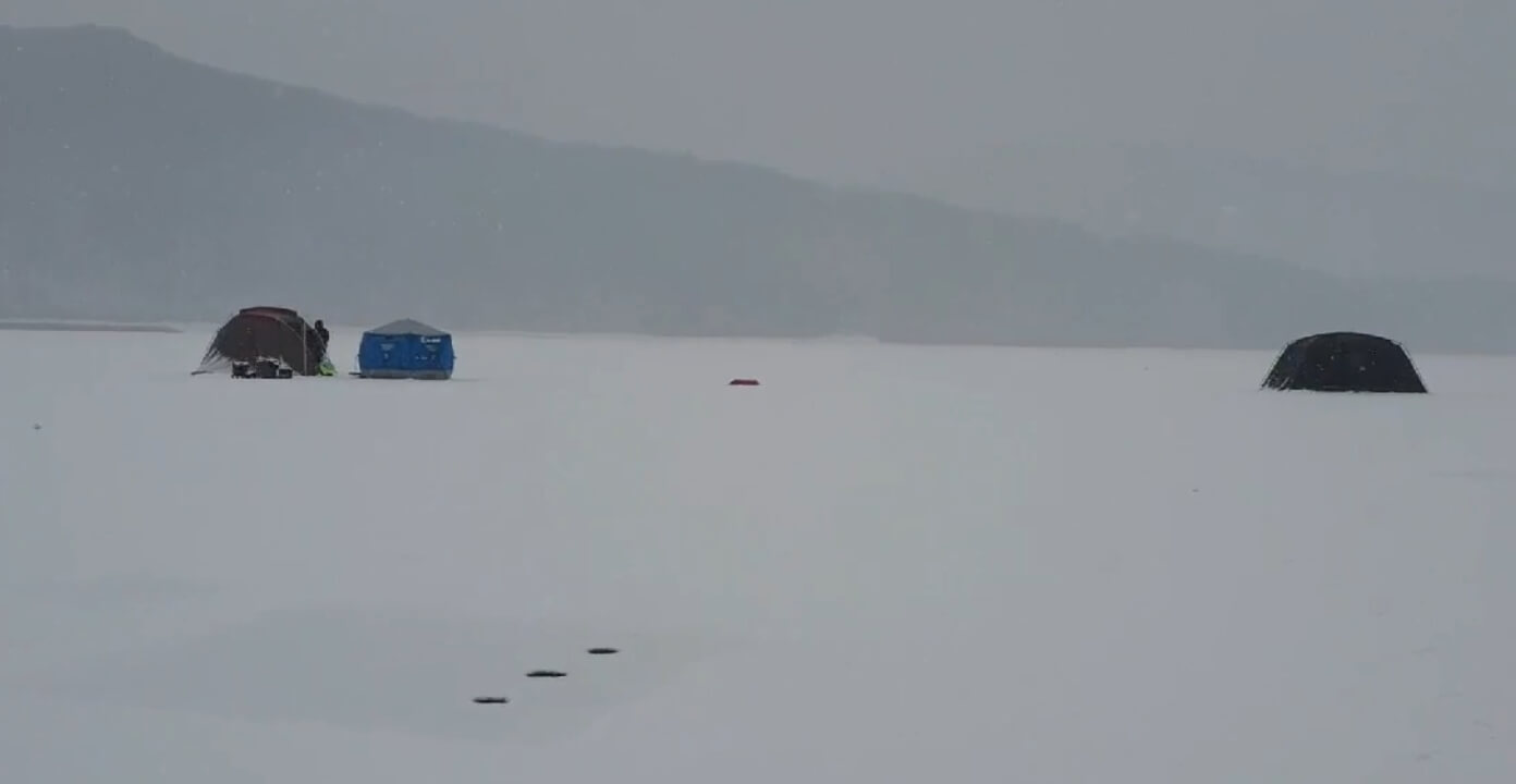 겨울철 얼어붙은 호수 위에 설치된 낚시 텐트들. 눈이 덮인 평야와 낚시터의 고요한 풍경