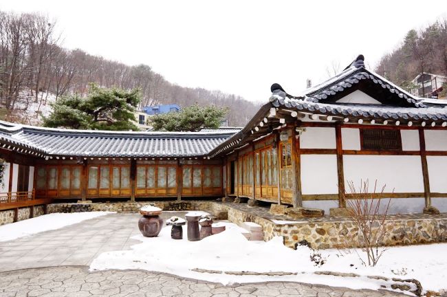 한옥 안채, 마당 한가운데 큰 장독 1, 뒤로는 울창한 숲, 산, 하얀 하늘,