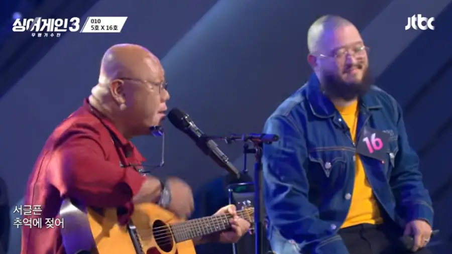 싱어게인3-
파란배경 빨간옷을 입고 노란색 기타를 치며 스탠딩마이크에 노래를하는 5호와 옆에서 흥얼대는 16호