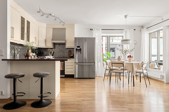 아파트 거실 풍경이다. 냉장고와 식탁이 있고 식탁 위에는 과일들과 꽃병이 있다.