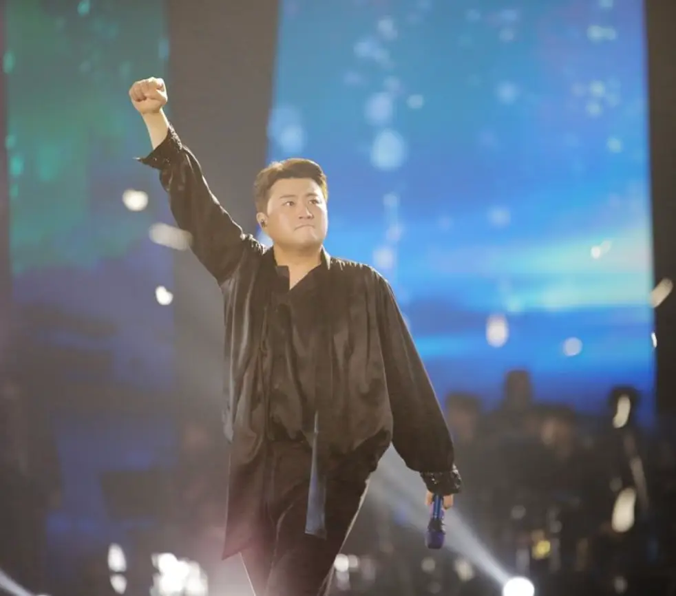 파란 무대배경 검은 블라우스를 입은 김호중이 오른손을 주먹쥔채 번쩍들고 있는 모습